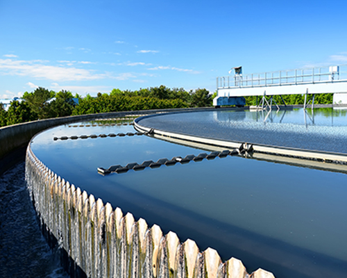 Circular clarifier with water flowing over its weir under a blue sky