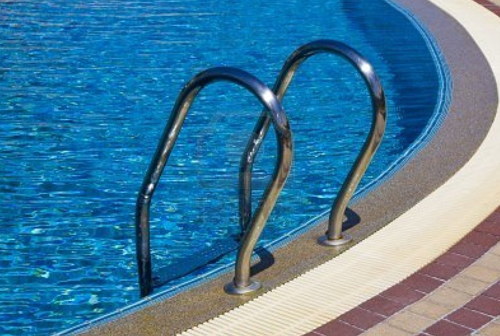 Stainless-steel ladder at the edge of a blue swimming pool
